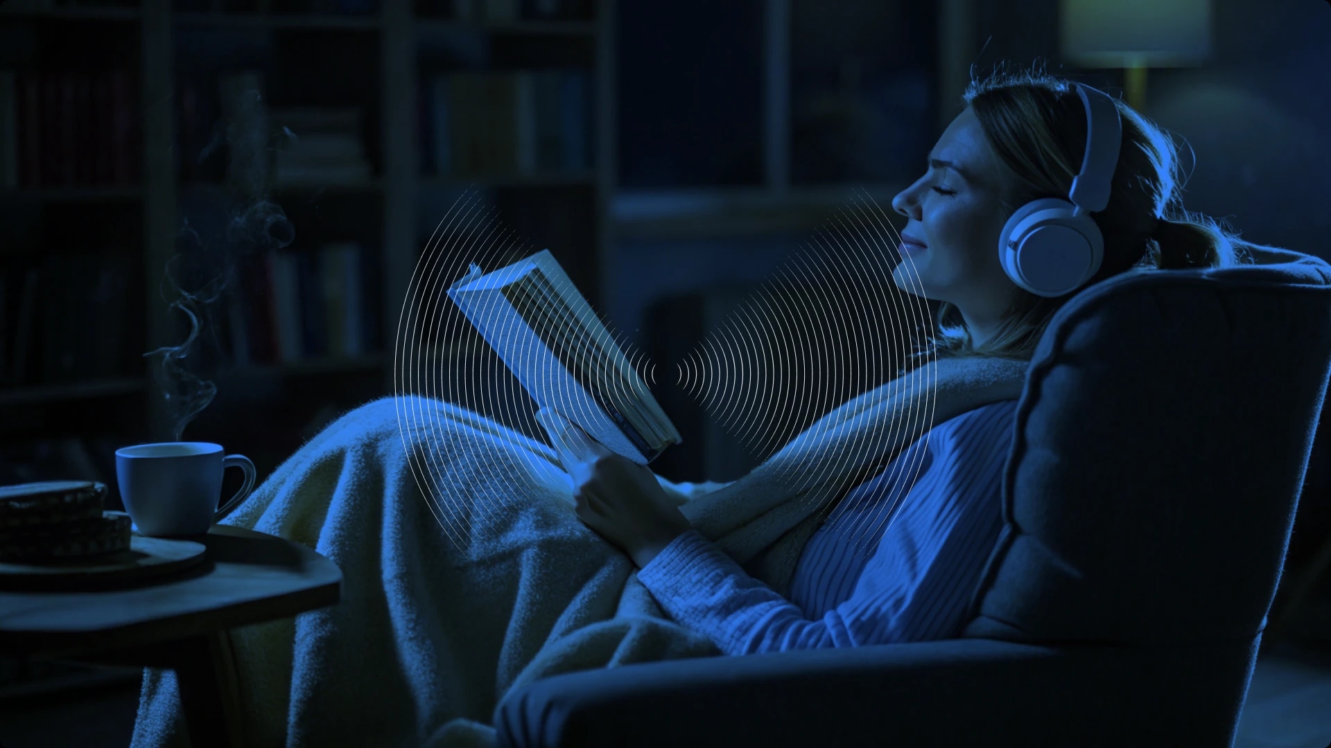 A woman relaxing in a chair, listening to music with headphones, reading a book, and enjoying a hot beverage in a cozy, dimly lit room.